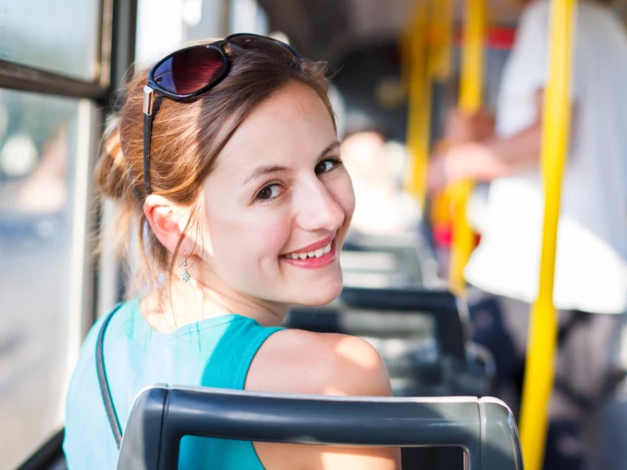 Junge Frau sitzt in einem Verkehrsmittel und schaut über ihre Schulter zurück