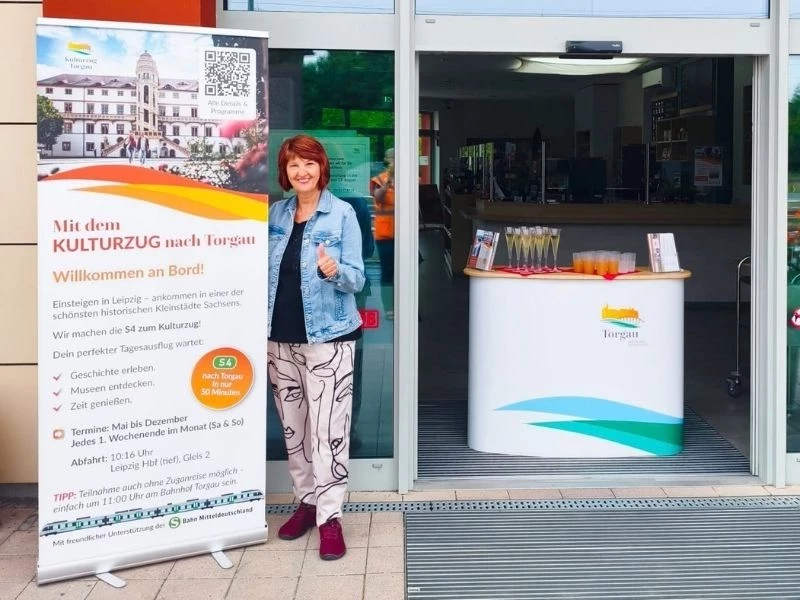 Eine Frau steht neben einem Roll-up mit Infos zum Kulturzug Torgau