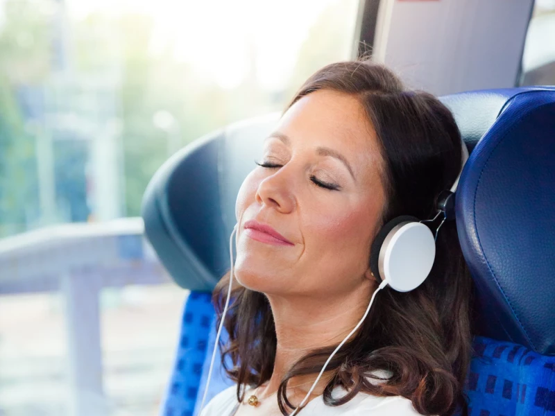 Frau mit Kopfhörern sitzt mit geschlossenen Augen im Zug