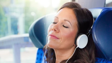 Frau mit Kopfhörern sitzt mit geschlossenen Augen im Zug