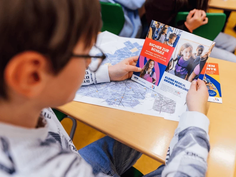 Ein Kind liest sich den Flyer "Sicher zur Schule" durch