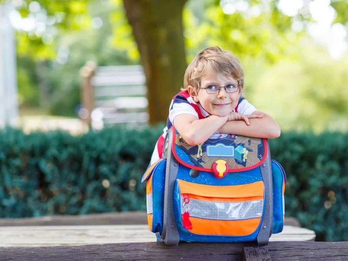 Schulkind stützt sich auf dem Schulranzen ab und lächelt