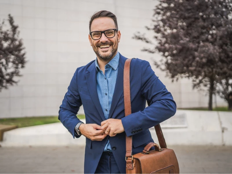 Mann im Anzug und mit brauner Umhängetasche lacht